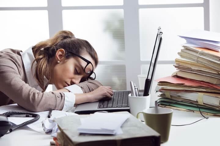 a fatigued worker sitting on a messy desk and sleeping