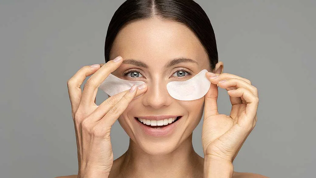 a woman putting eye pads under her eyes 